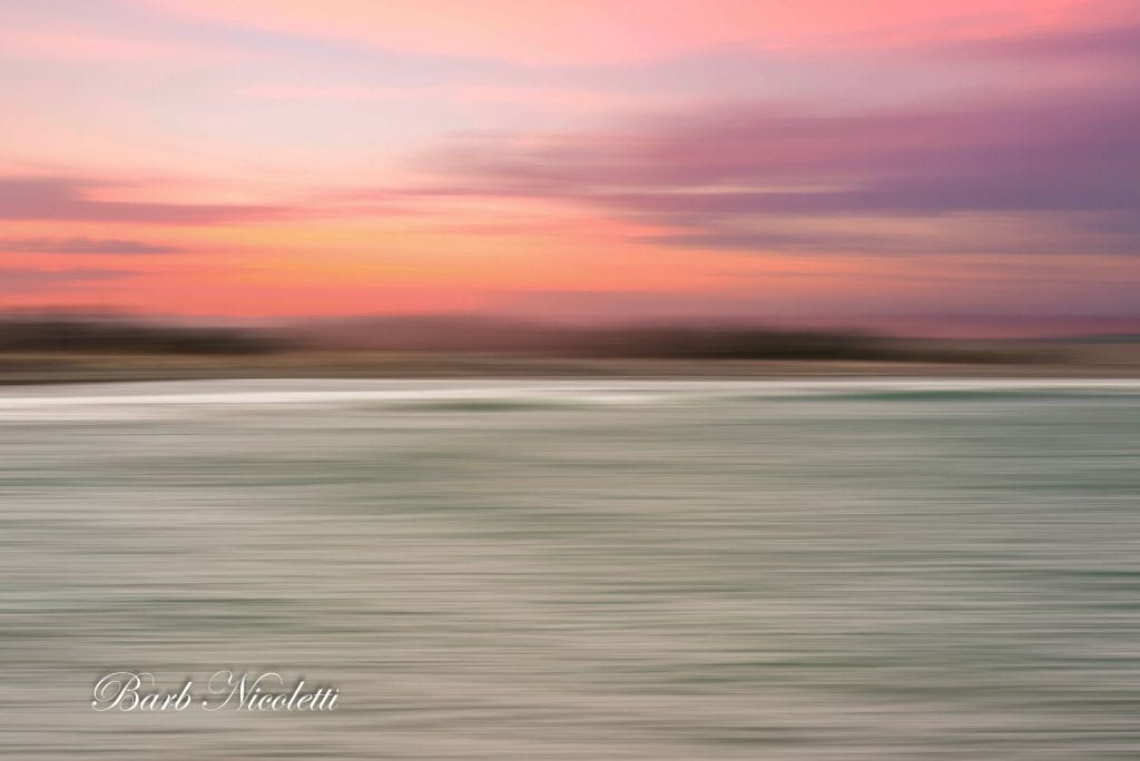 Blurred beach and ocean with a pink sky.