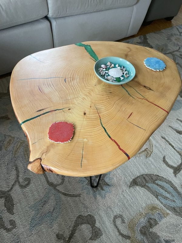 A round coffee table made from a large slice of pinewood. Two coasters and a bowl of shells sit on the table.
