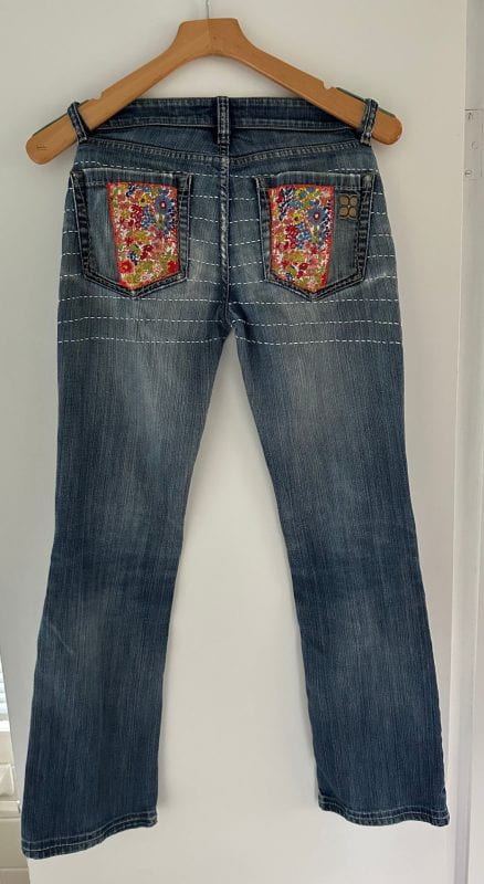 A pair of jeans with a bright floral pattern sewn onto the back pocket squares.