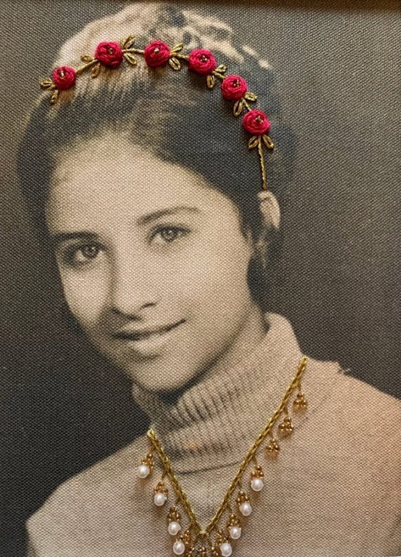 Black and white photo of a young woman wearing an embroidered tiara with golden thread and dark red rosettes. She is also wearing a necklace with embroidered with golden thread and gold and pearl beads.