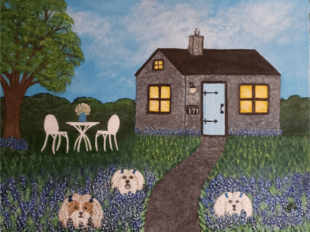 A small gray cottage with lights on in its windows. The yard has a white garden table and chair set. The foreground has three small white dogs playing among blue and purple flowers.