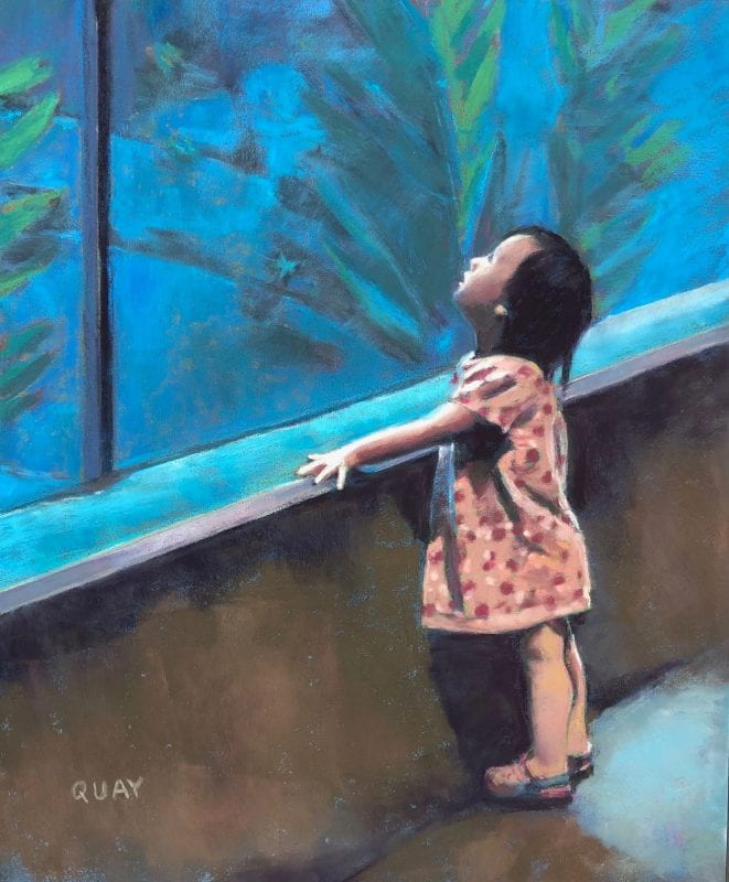 A very little girl with short black hair and a pink dress is looking up at the window of a very large zoo aquarium with an expression of wonder on her face.