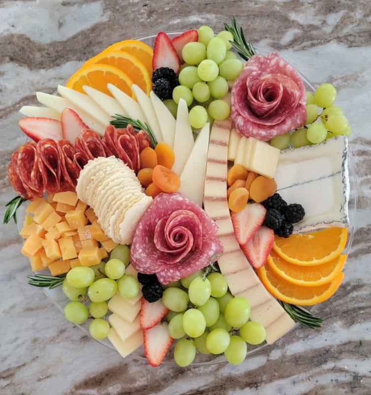 Cured meats placed as flower blooms and yellow cheese, crackers, apricots and orange slices which give a warm yellow color tone to the board. Sliced strawberries, berries, grapes, and rosemary leaves add some different color.