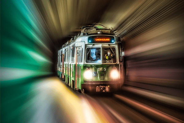 A Green Line train in the midst of a green and gold vortex of color. The train's headlights are illuminated and its destination sign reads "Union Square."