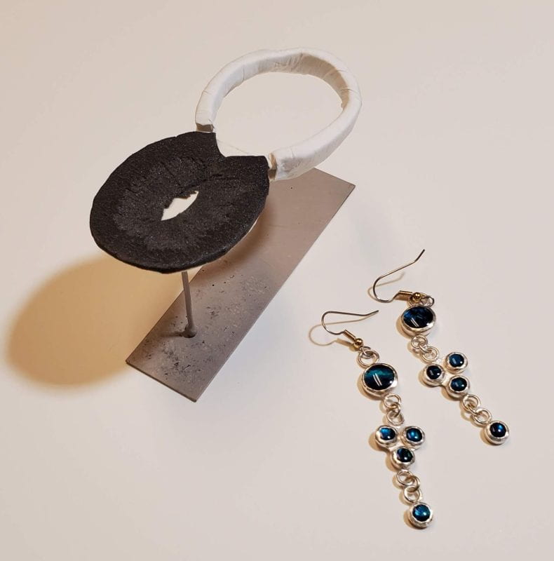 Support for magnifying glass lifted to fit over the edge of a book, and a pair of silver and blue earrings.