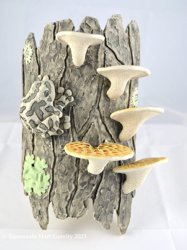 Porcelain sculpture of a tree trunk with mushrooms, lichen, and a gray treefrog.