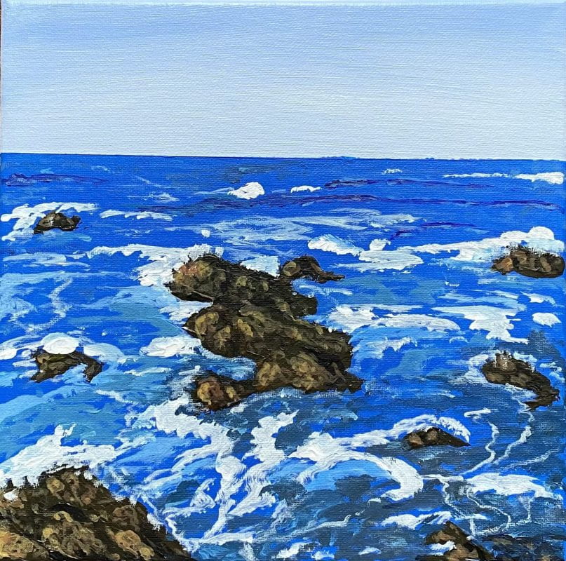 Churning, vibrant blue ocean water with rocks and a calm blue sky.