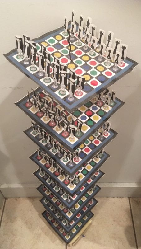 A picture of a complicated customized set of chessboards. Eight boards are stacked atop each other; each board has color-coded circles in the usual black and white spaces. The pieces are black and white paper in clear stands. Each board has a full complement of 32 pieces.