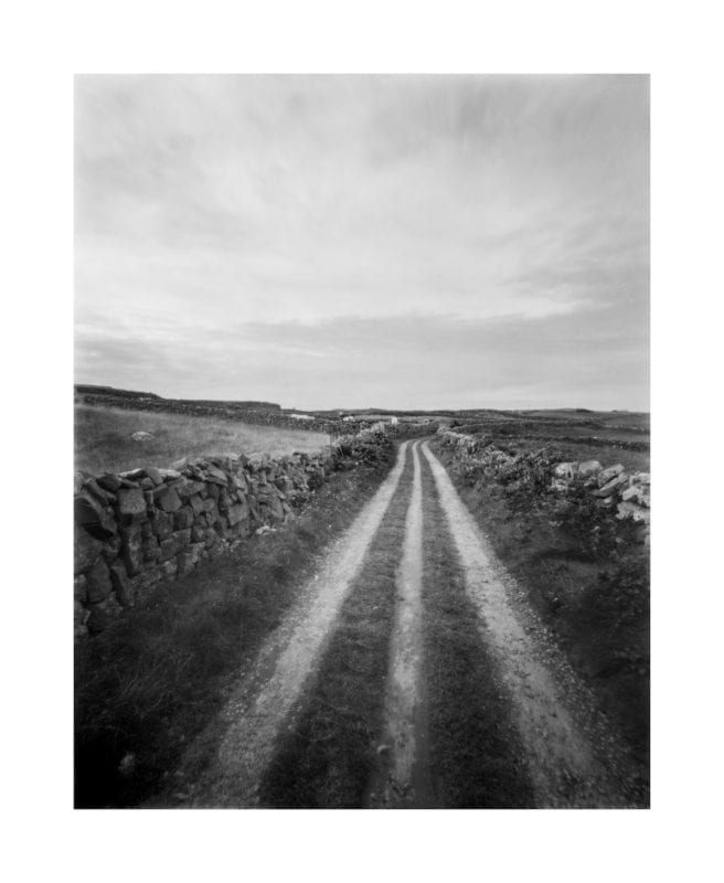 A timeless rural road in Ireland flanked by old stone walls in black and white.