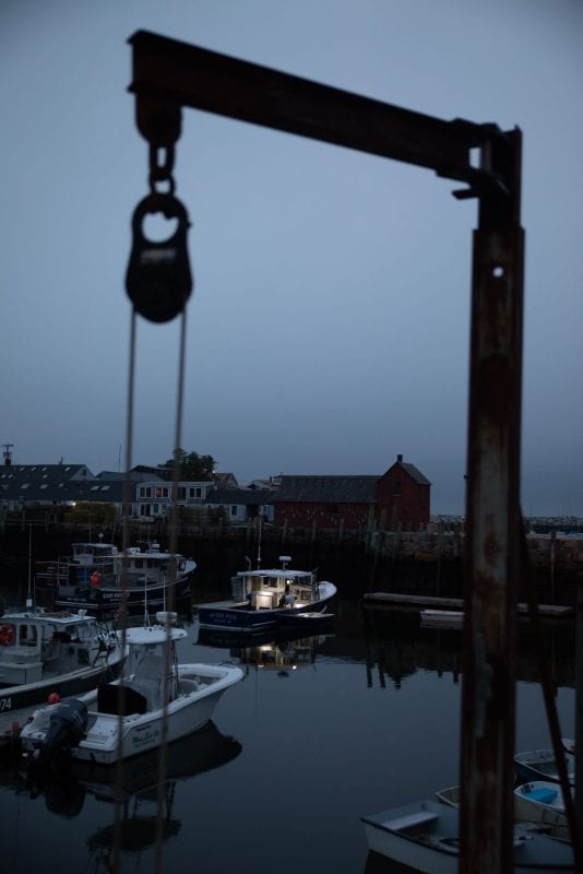 Bradley Wharf in Rockport, in heavy fog and low light. A single light illuminates from a boat as a fisherman prepares for the day.