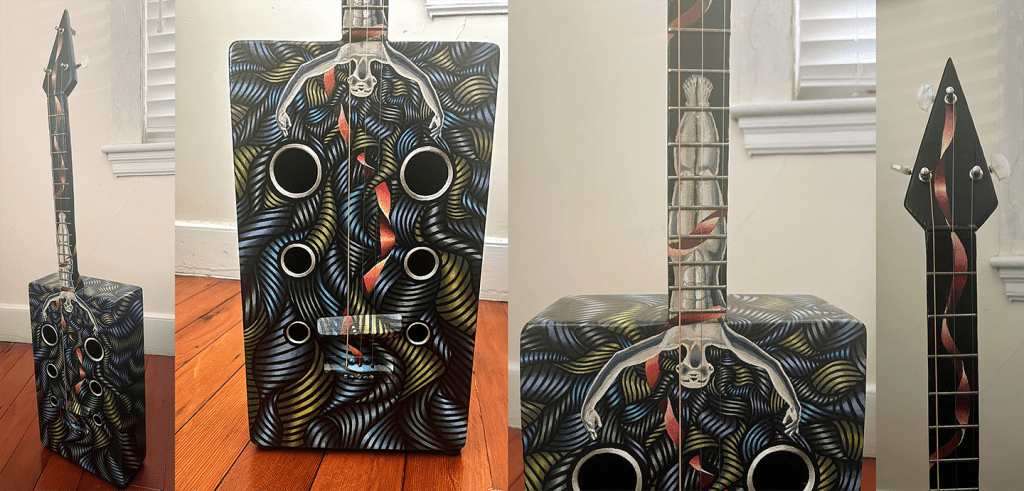 A box shaped guitar with a stylized painting of a figure on it.