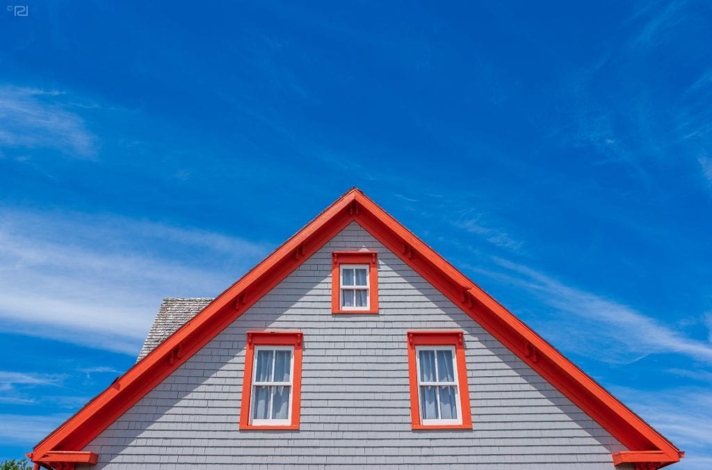 A house gable against a blue sky. Trims in contrasting orange color. Copy space beyond the rooftop.